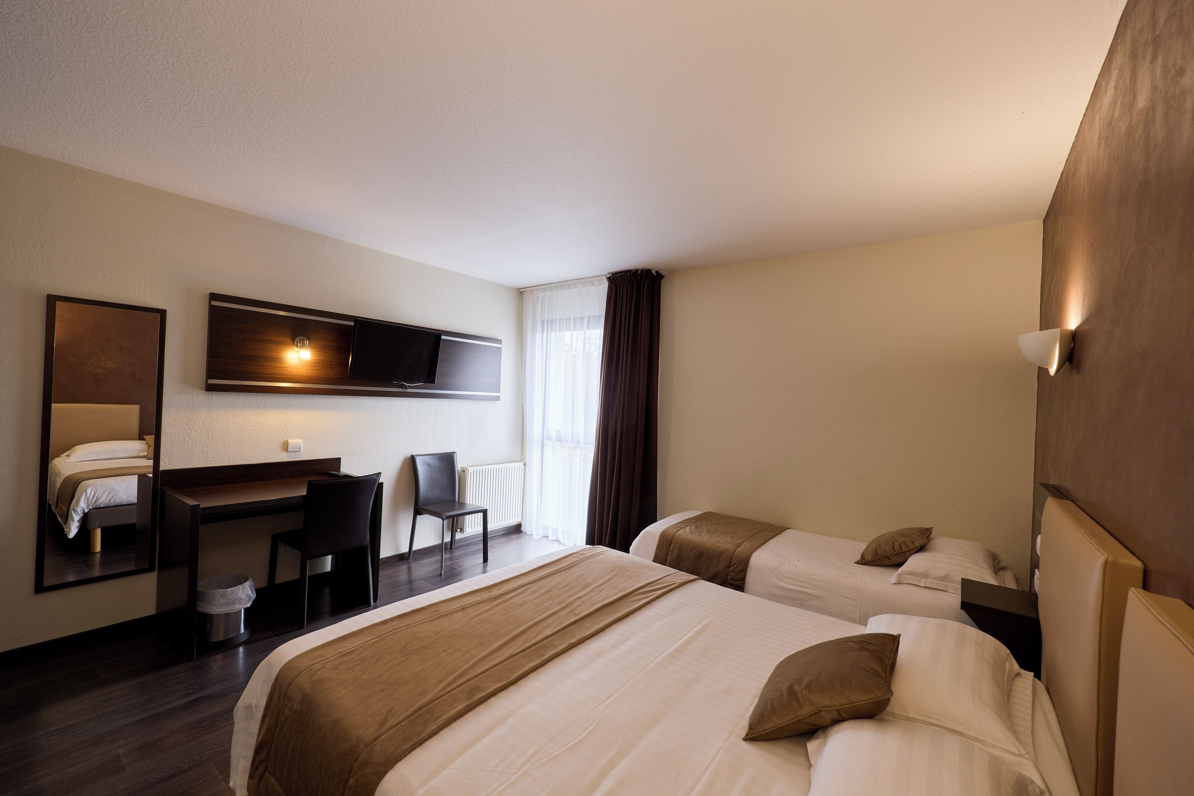 Una habitación de hotel con dos camas, un escritorio, una silla, un televisor y un espejo grande.