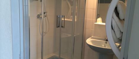 Une douche fermée par des parois en verre, dotée d’un pommeau de douche à main, d’un lavabo blanc et d’un porte-serviettes.