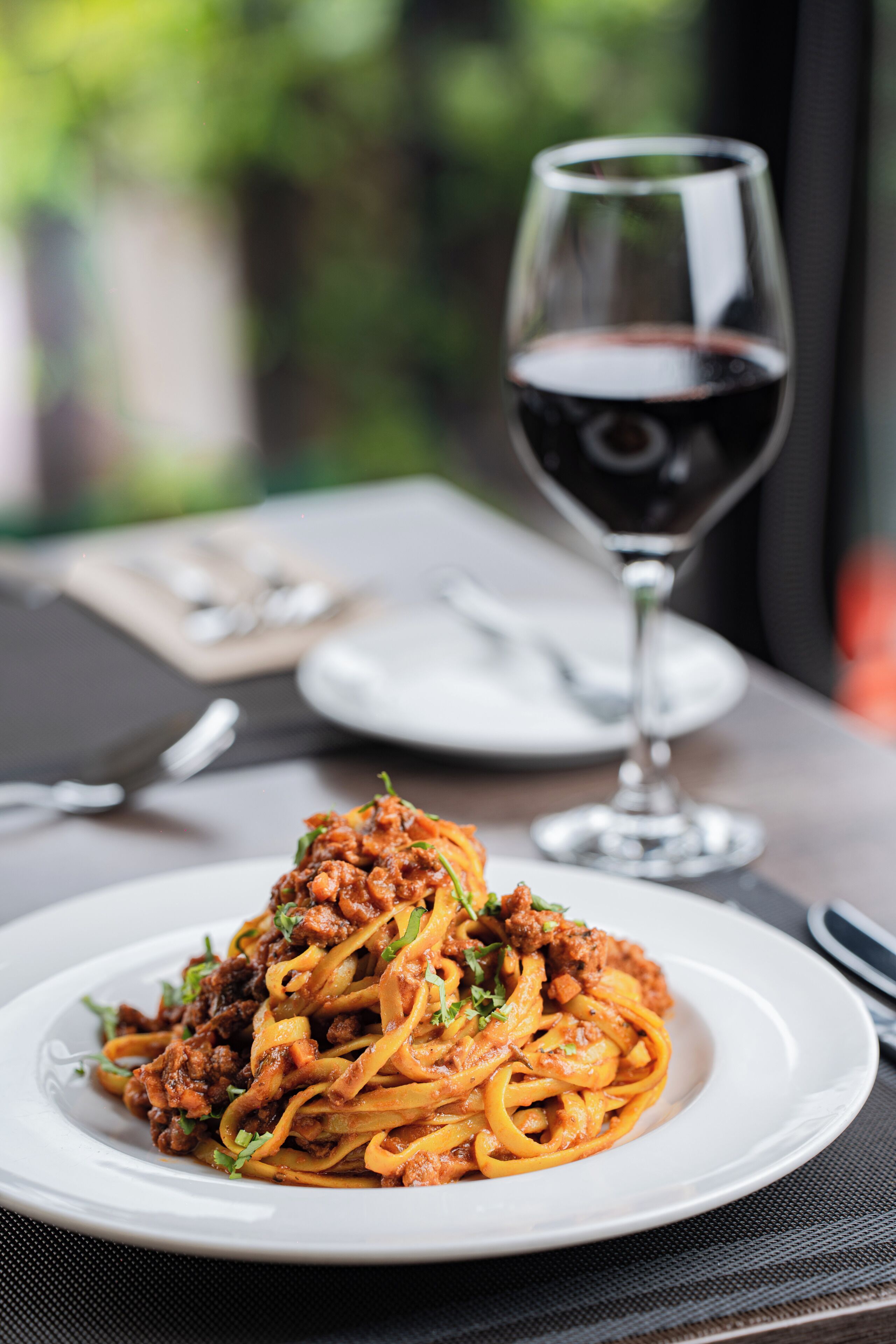 Eine Spaghetti-Kruste mit Fleischsoße und ein Glas Rotwein auf einem Tisch.