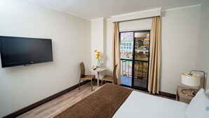 Quarto de hotel com cama, televisão, escrivaninha e cadeira, janela com cortinas e vista para o exterior.