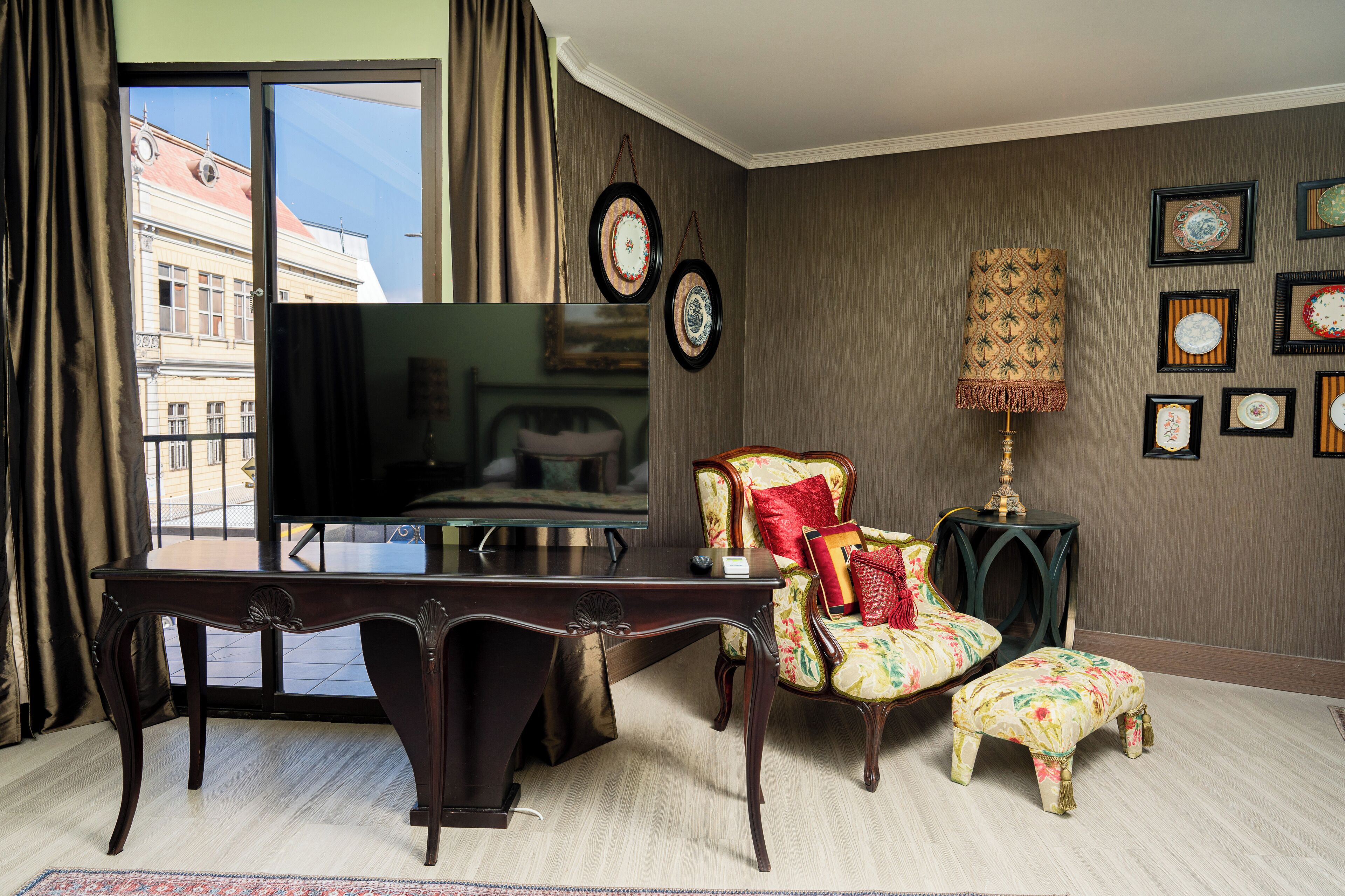 A room with a large window, a desk, a chair, and a television.