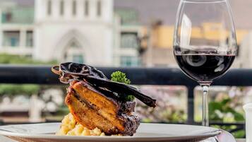 A plate of food with a glass of red wine on a balcony with a view of a building.