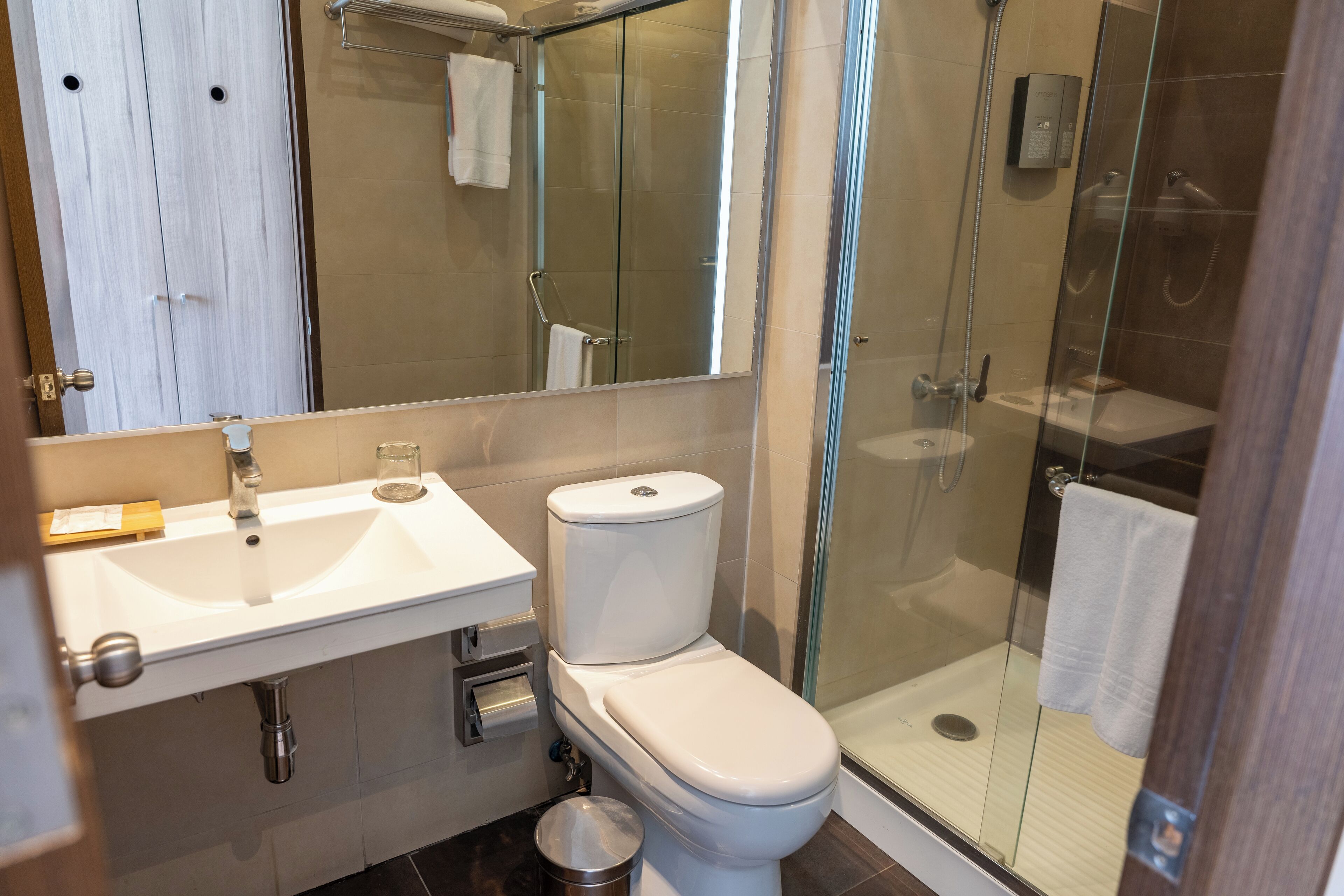 Un baño moderno con ducha de vidrio, lavamanos blanco y retrete.