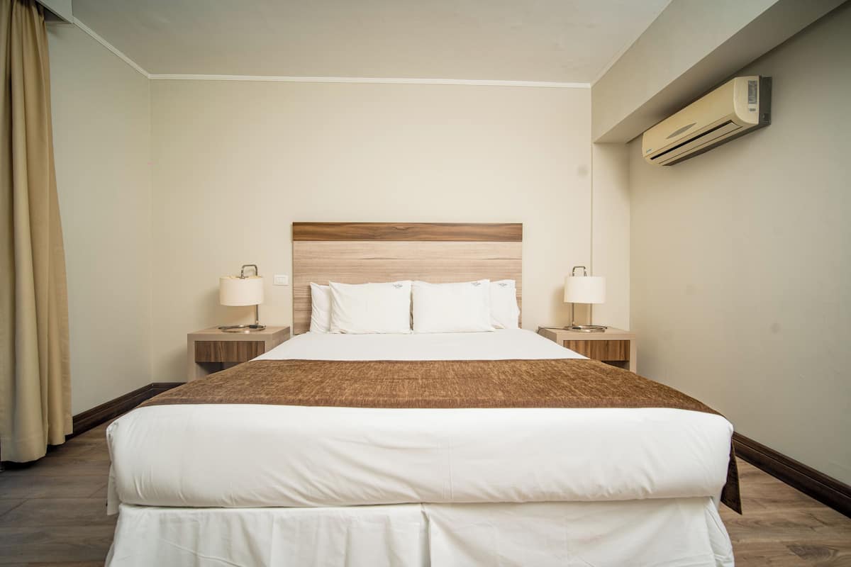 Hotellihuone, jossa on suuri sänky, kaksi yöpöytää valaisimineen, sängynpääty ja ilmastointilaite seinässä.