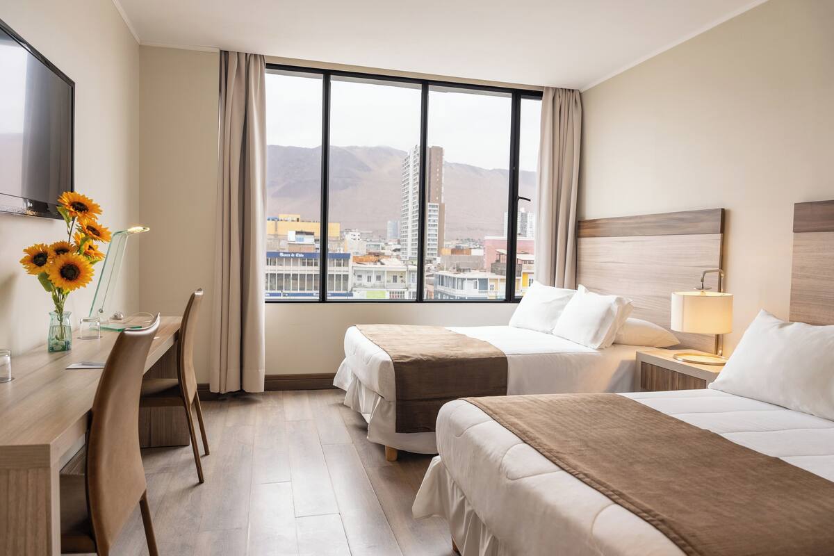 Hotellihuone, jossa on kaksi sänkyä, työpöytä, tuoli, televisio ja suuri ikkuna, josta on näkymä kaupunkiin.