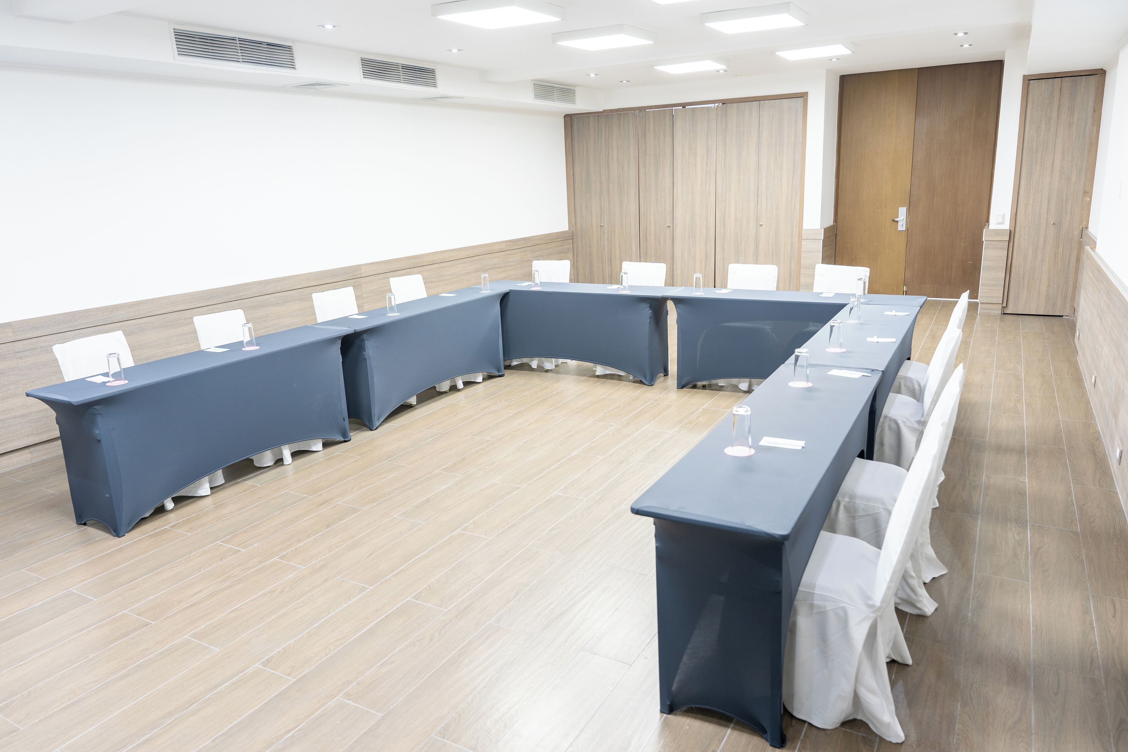 Un salón de conferencias con una larga mesa, sillas blancas y suelo de madera.