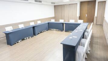 Un salón de conferencias con una larga mesa, sillas blancas y suelo de madera.