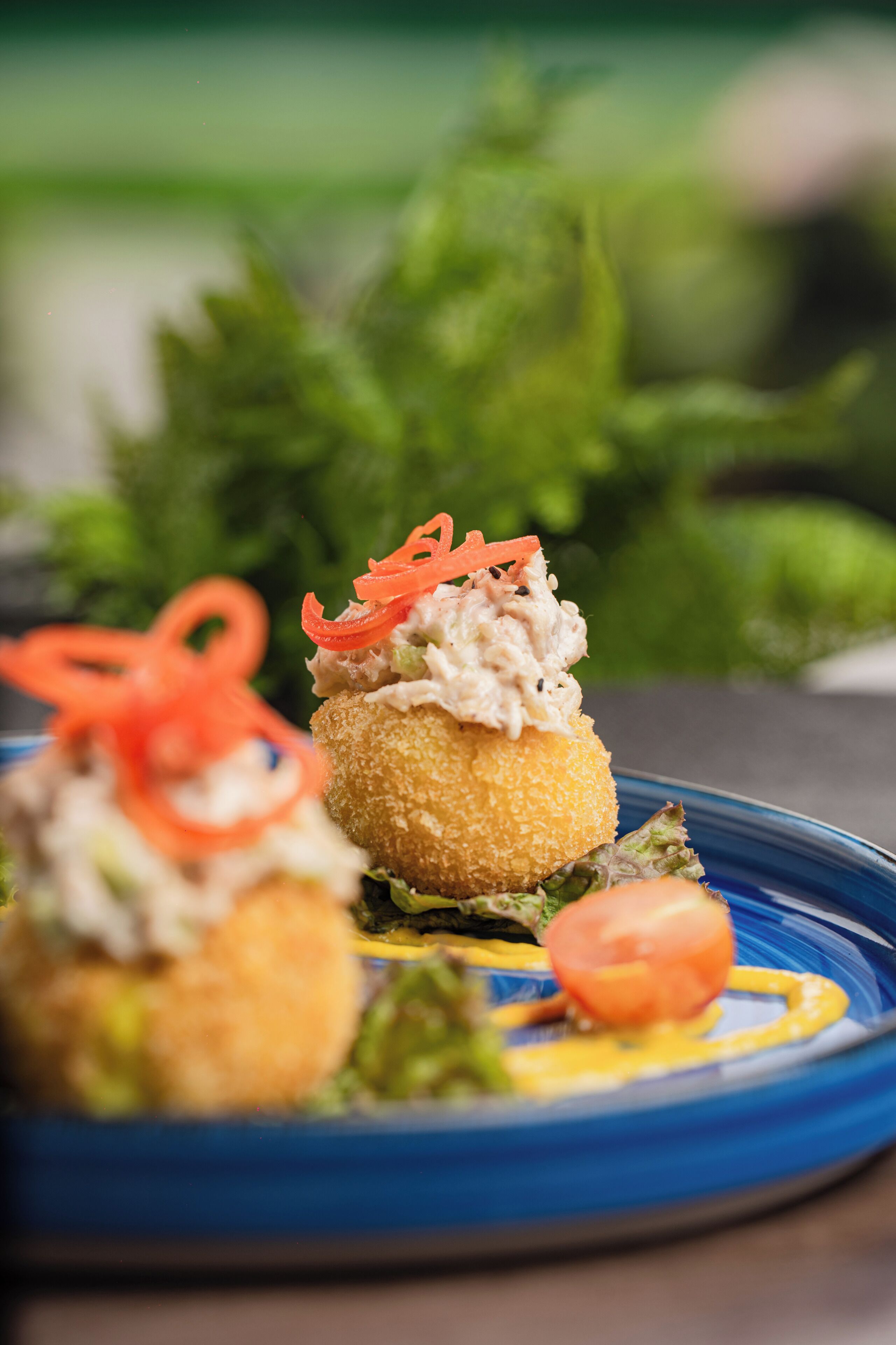 A blue plate with a food item topped with a creamy substance and garnished with carrot slices, accompanied by a small tomato and green leaves.