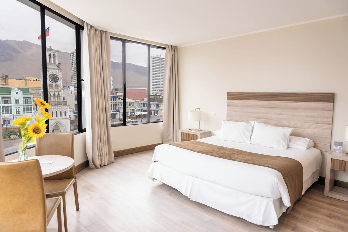 Hotellihuone, jossa on suuri ikkuna, sänky, yöpöytä ja tuoli.