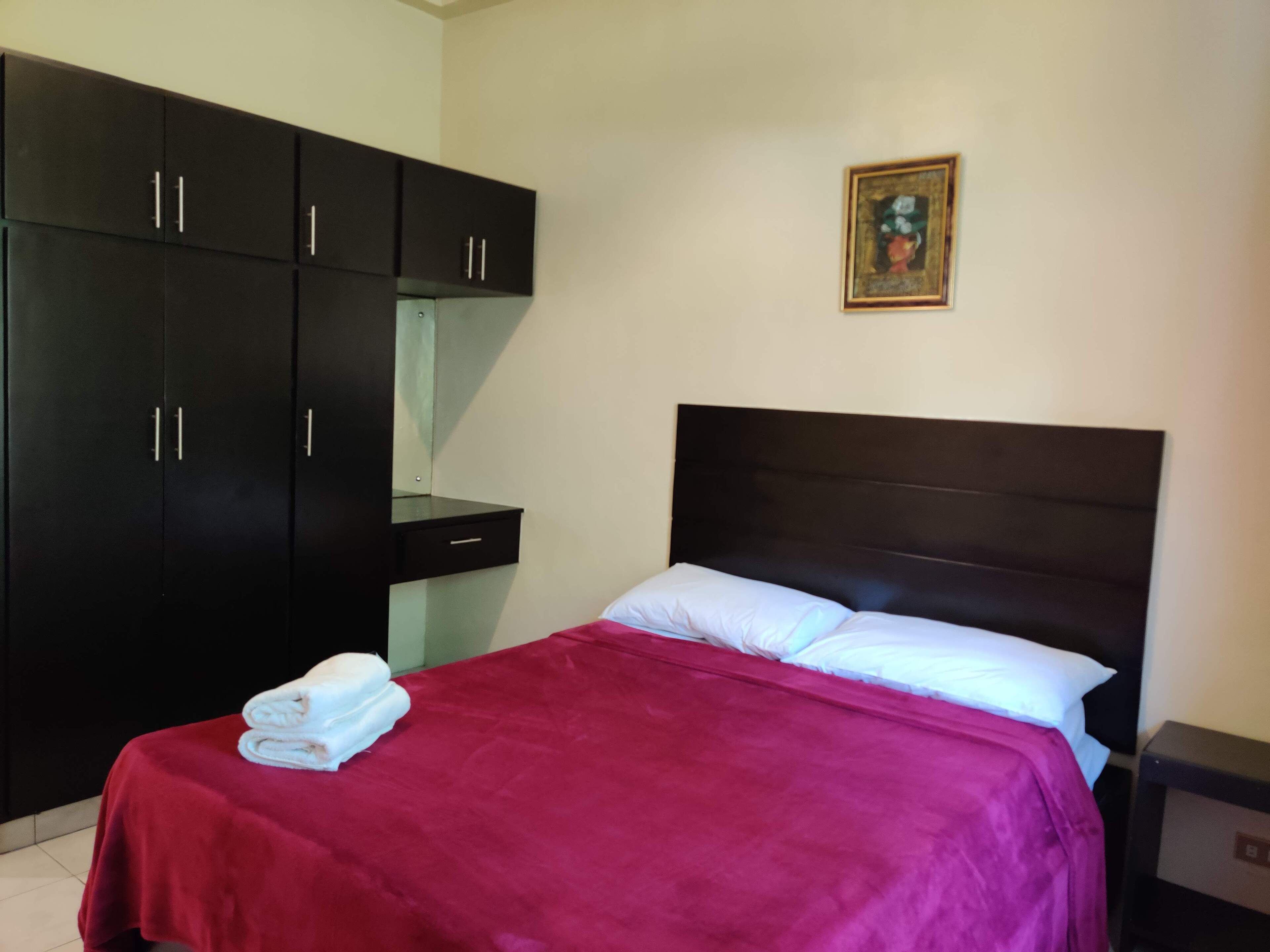 A bedroom with a bed, a nightstand, a wardrobe, and a painting on the wall.