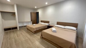 Une chambre d’hôtel avec deux lits, une armoire en bois, un banc et une étagère fixée au mur.