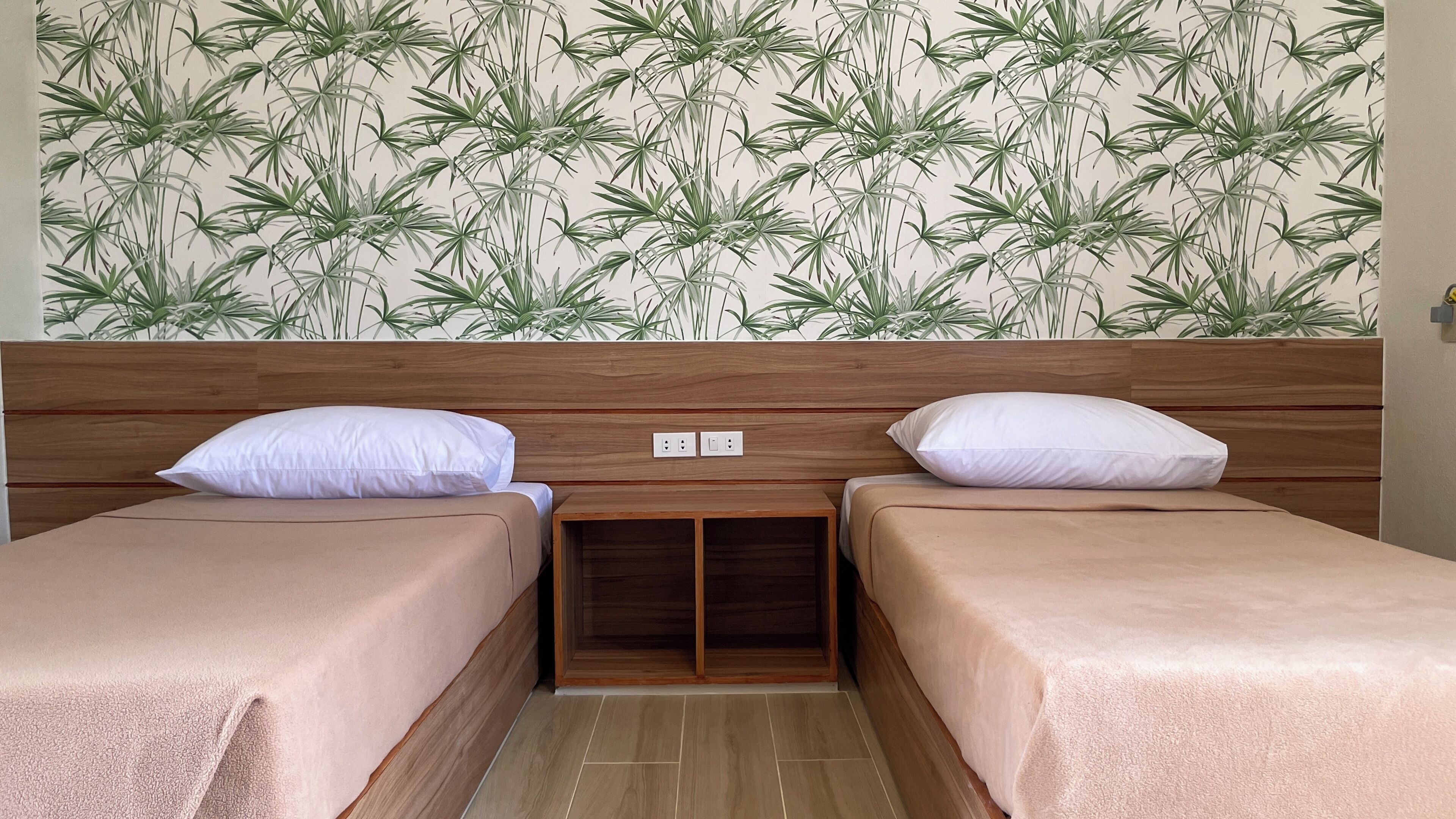 Habitación con dos camas, cabecero de madera y pared con diseño de hojas de bambú.