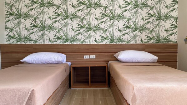Habitación con dos camas, cabecero de madera y pared con diseño de hojas de bambú.