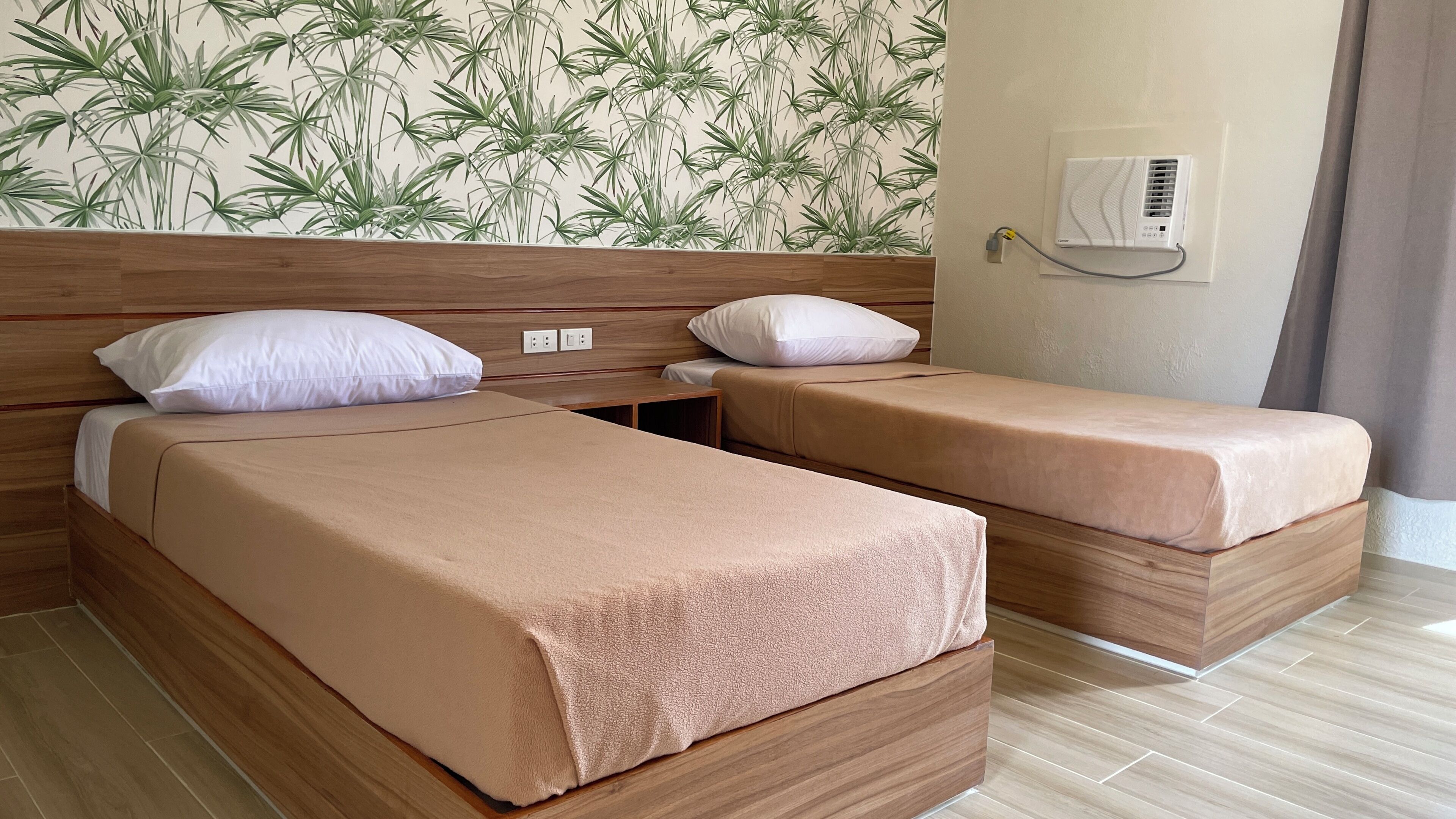 A hotel room with two beds, a wooden headboard, a wall air conditioner, and a patterned wallpaper.