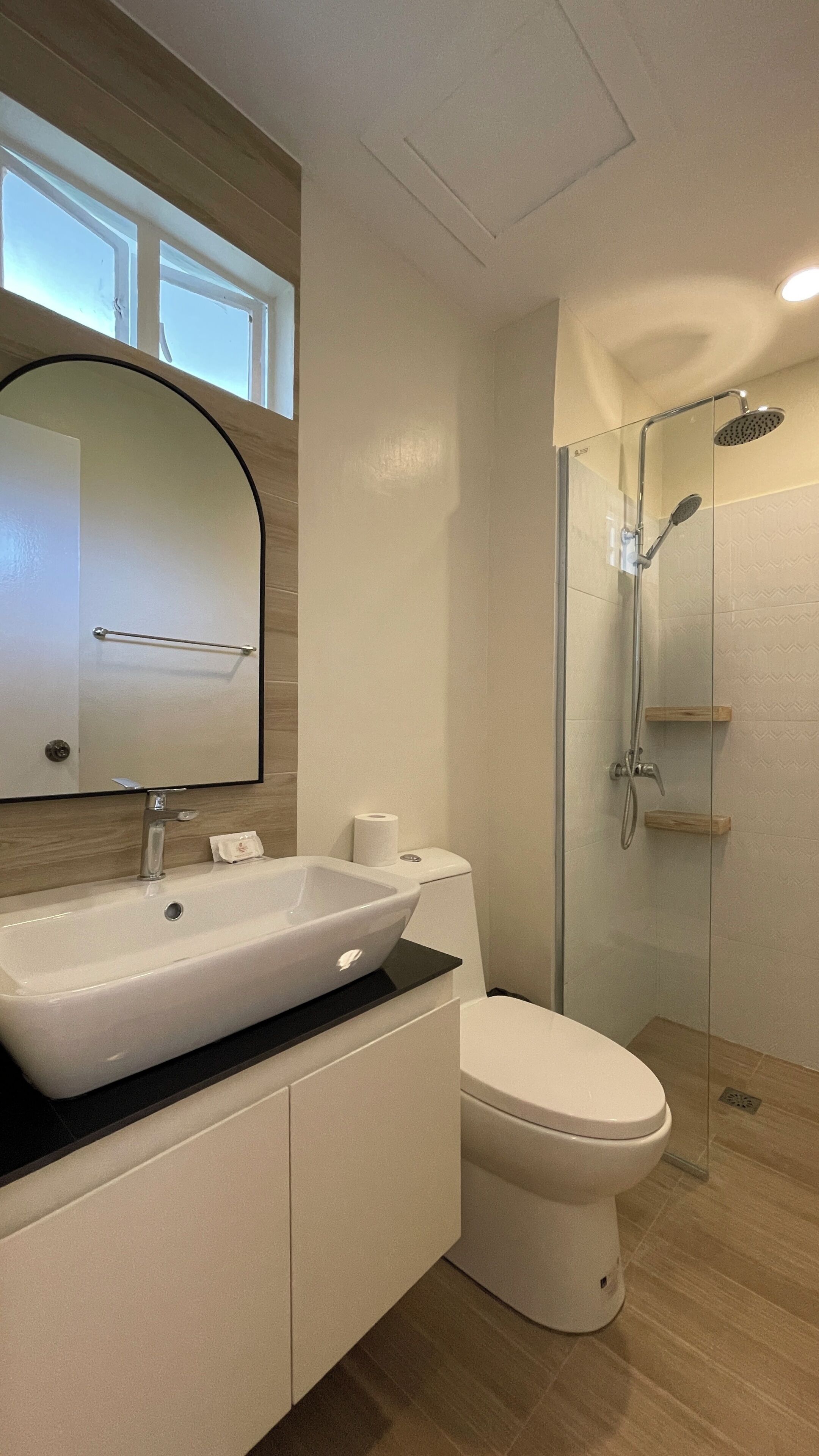 A bathroom with a white sink, mirror, toilet, and a glass-enclosed shower area.