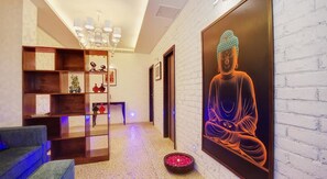 A modern interior with a Buddha statue, a wooden bookshelf, and a chandelier. - Palm Springs Stays (New Delhi)
