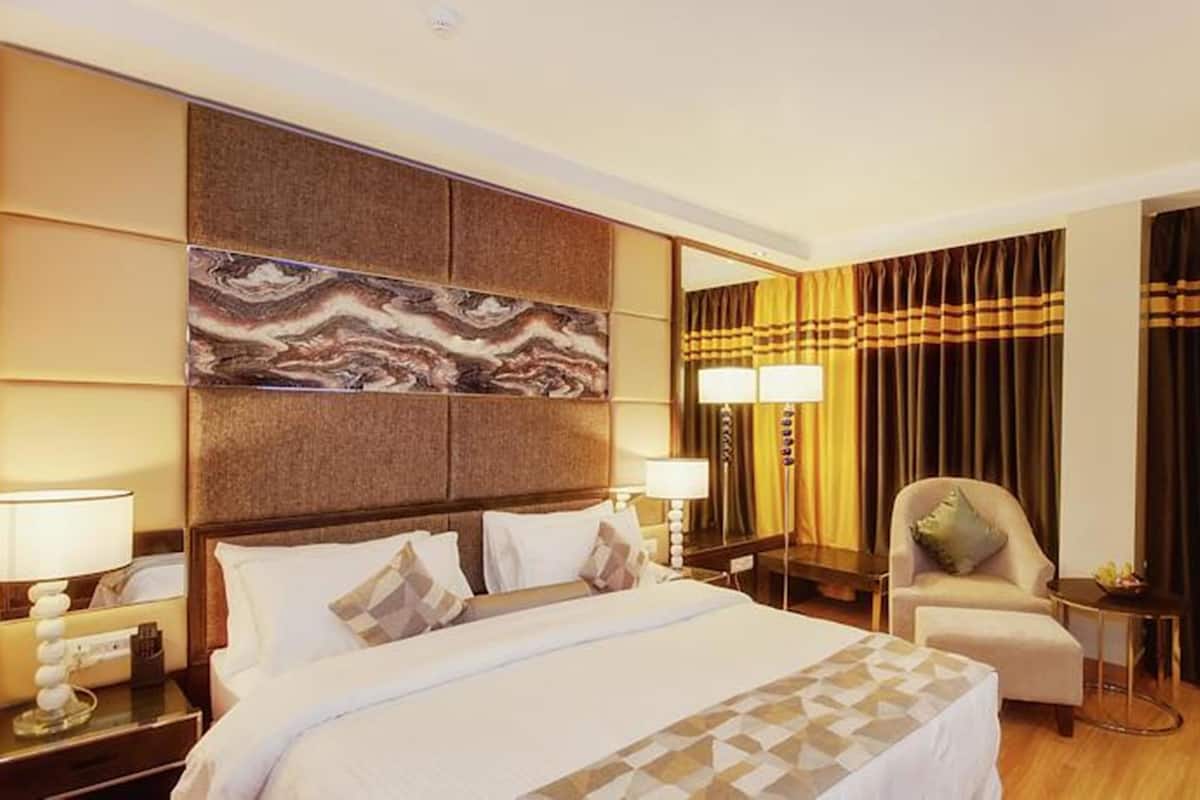 A hotel room with a large bed, two bedside lamps, a chair, a desk, and a large mirror.