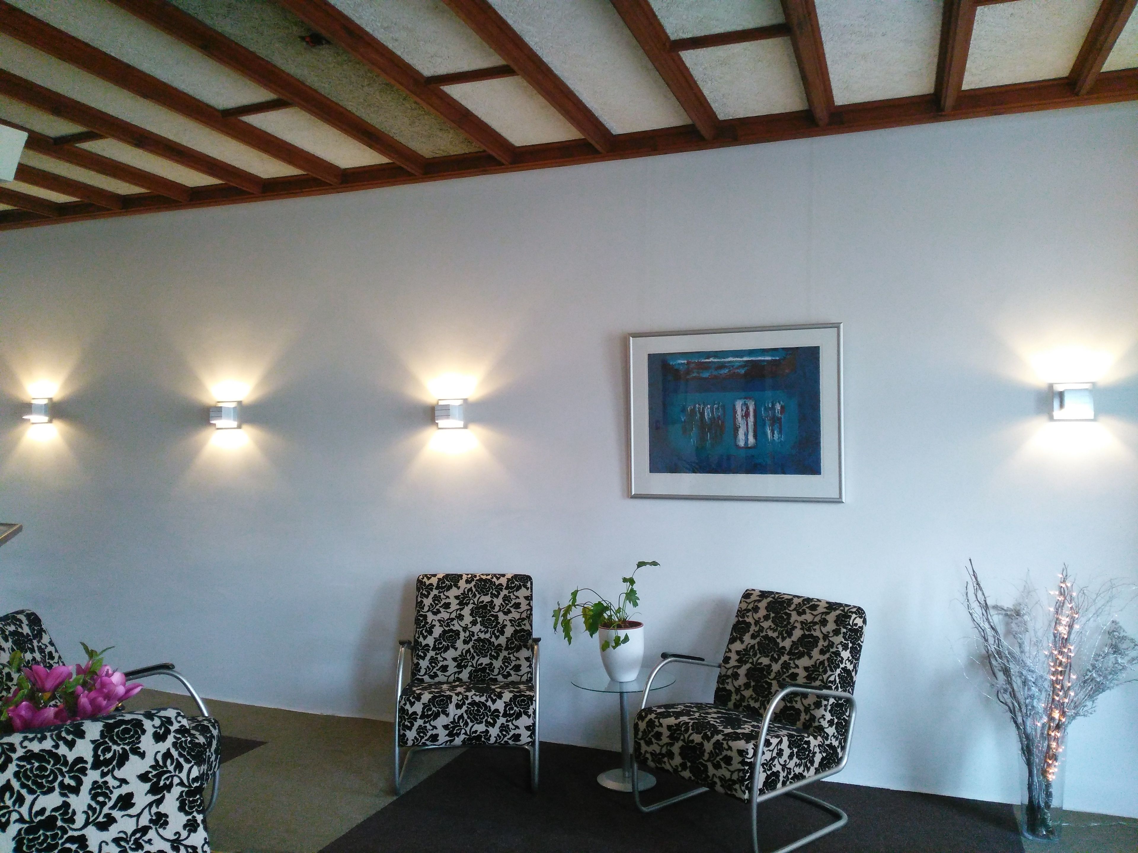 A waiting area with two patterned chairs, a small table with a plant, and a framed artwork on the wall.
