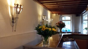 Une cuisine avec un plan de travail en bois, un évier et un vase rempli de fleurs jaunes. On y trouve également des appliques murales et une fenêtre avec des rideaux.
