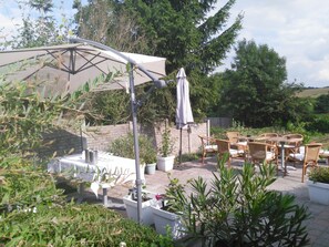 An outdoor patio area with a table and chairs, surrounded by potted plants and a large umbrella.