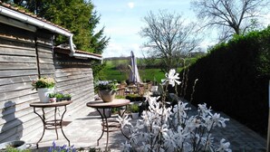 Une terrasse avec des tables et des chaises en bois, entourée de plantes et de fleurs en pot.
