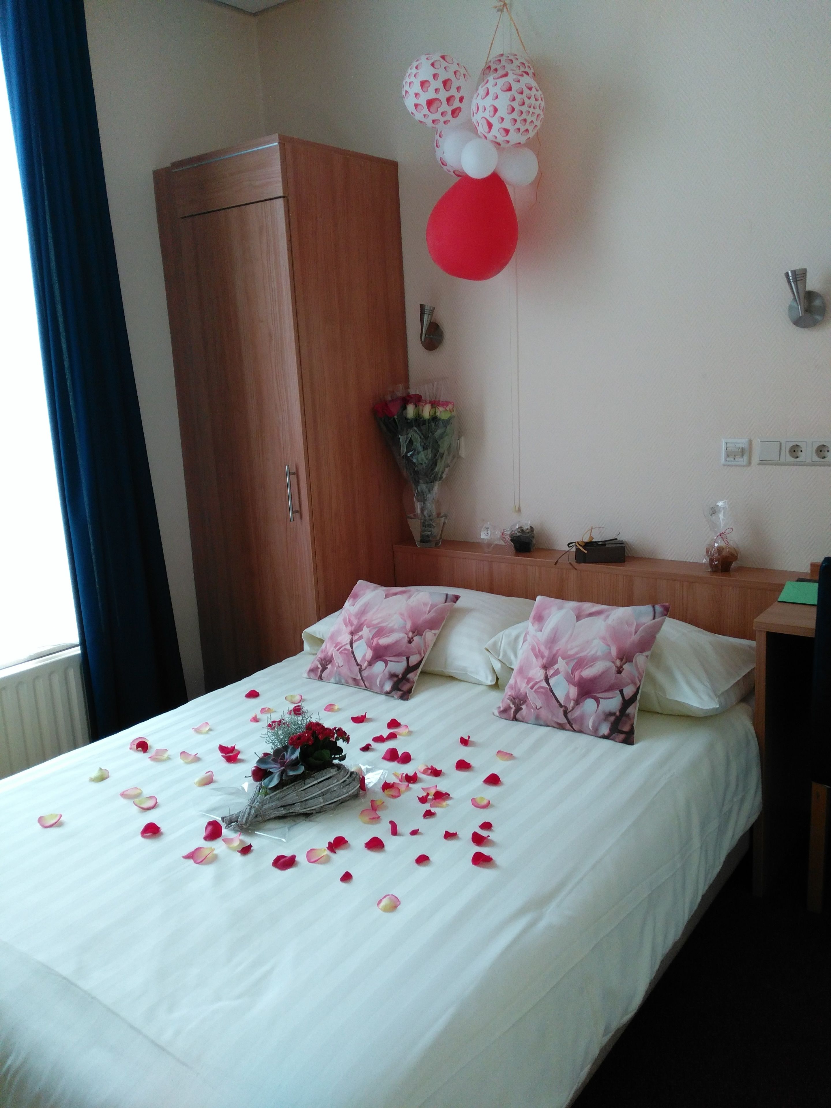A hotel room with a bed, pillows, a bouquet of flowers, and a wall decoration.