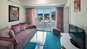 A living room with a sofa, a coffee table, a TV, and a balcony with a view of the sea. - Bella Vista (Becici)