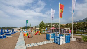 A beachside playground with play structures, a sandy path, and flags. - Bella Vista (Becici)
