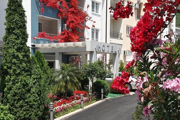 A hotel entrance with a sign, surrounded by lush greenery and vibrant red flowers. - Bella Vista (Becici)