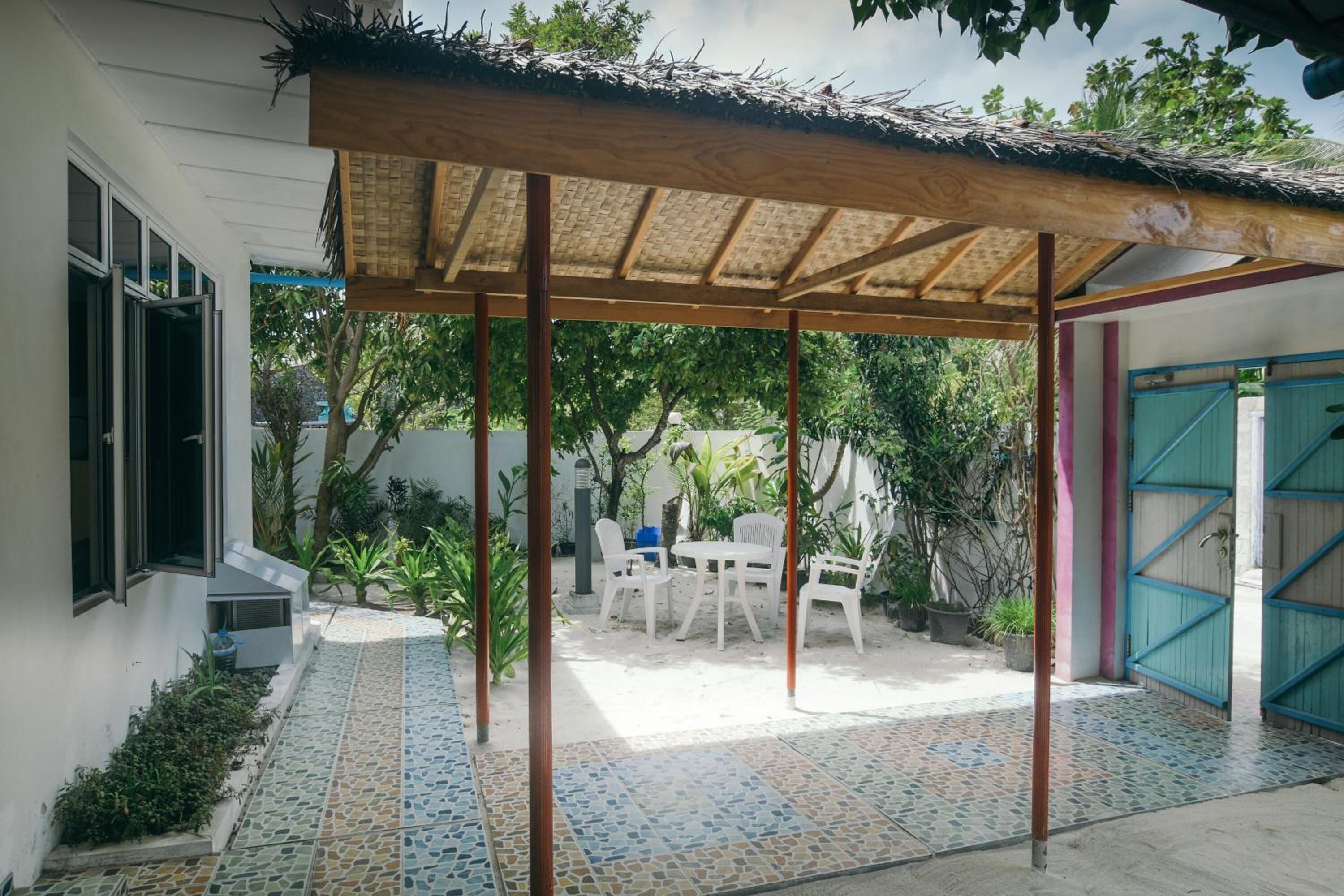 Un patio couvert avec un sol carrelé, une table et des chaises, et un portail bleu.