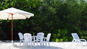 A beach setting with a white umbrella, white plastic chairs, and a table. - Azoush Tourist Guesthouse (Fulhadhoo)