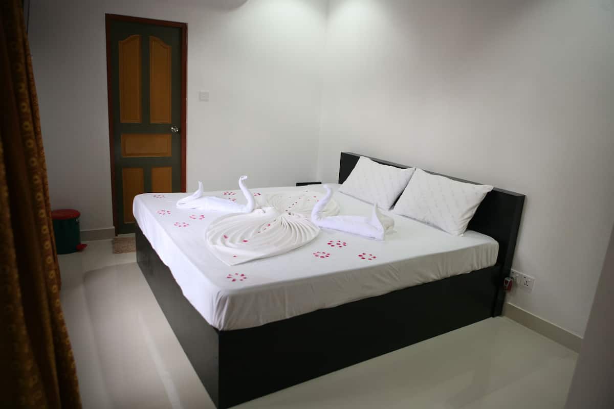 A neatly made bed with white linens and decorative swan-shaped towels, a dark headboard, and a closed door in the background.