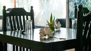 A dining table with chairs, a vase with a plant, and a glass. - Azoush Tourist Guesthouse (Fulhadhoo)