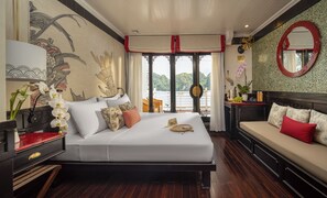 A hotel room with a bed, a sofa, a desk, and a large window with a view of the water.