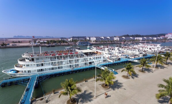A large white cruise ship docked at a pier with multiple decks and lifeboats visible.