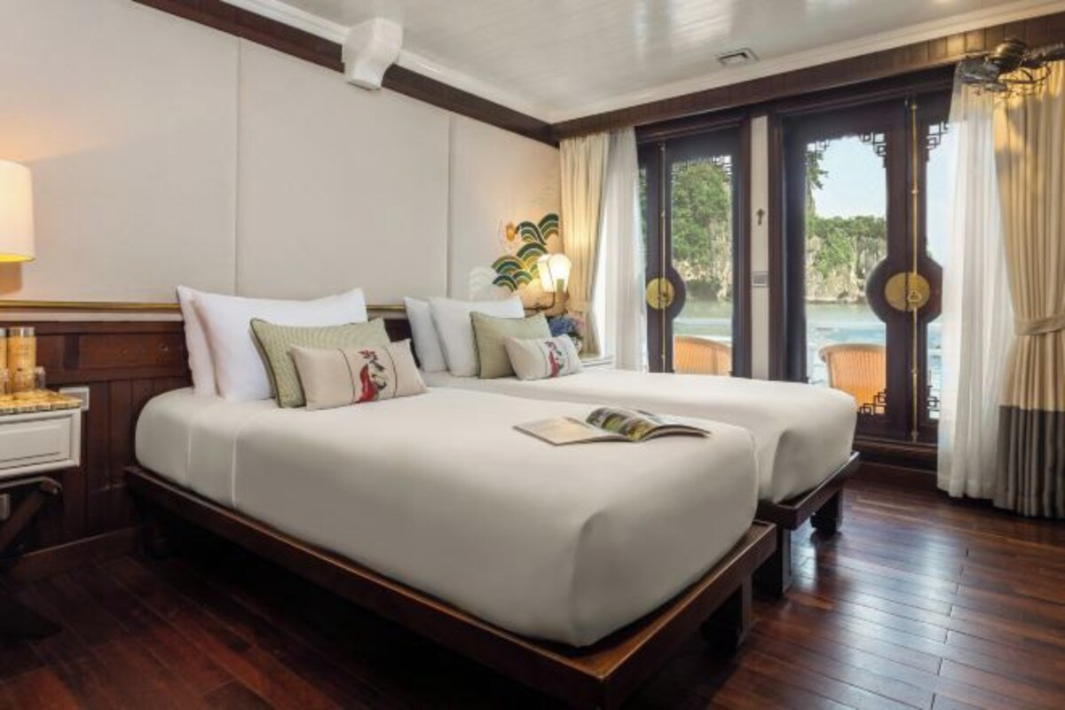 A double bed with a wooden frame, a bedside table with a lamp, and a view of the outdoors through a glass door.
