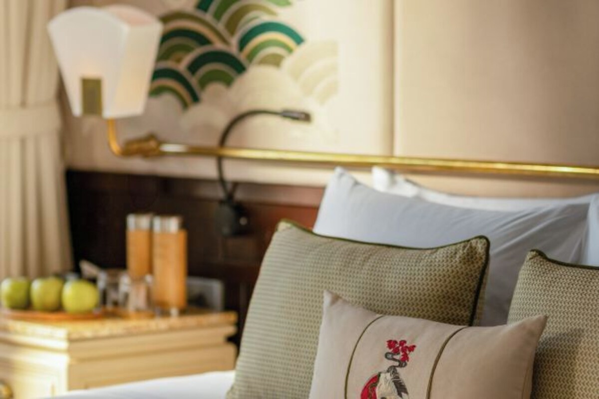 Una habitación de hotel con una cama, almohadas, una mesita de noche con lámpara y una pared decorada con una planta.