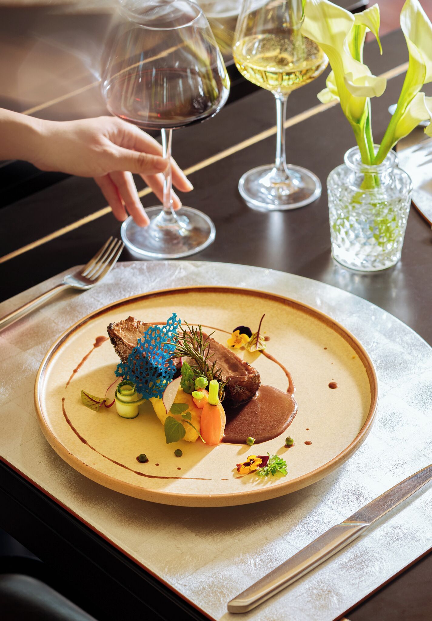 A dining table with a plate of food, a wine glass, and a vase with flowers.