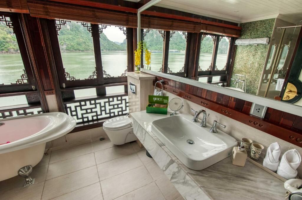 A bathroom with a bathtub, sink, and toilet, featuring a view of a river through large windows.