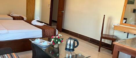 A hotel room with a bed, a glass coffee table with a kettle, a chair, and a desk with a mirror.