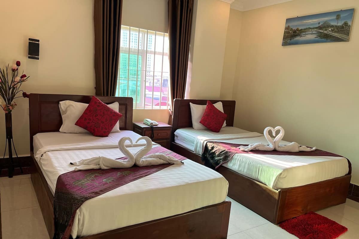 Habitación de hotel con dos camas, cada una con una decoración de toallas con forma de corazón, una mesita de noche, un jarrón con flores y un cuadro en la pared.