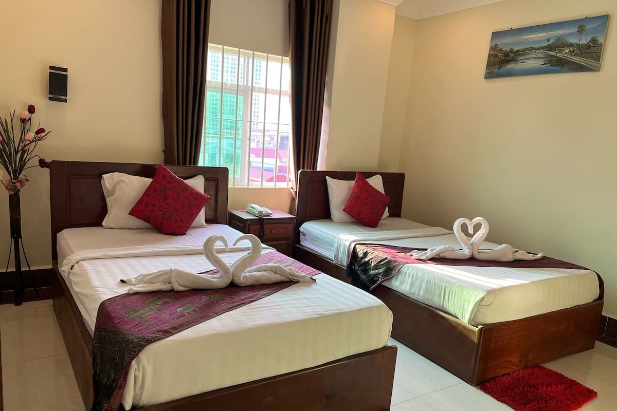 Habitación de hotel con dos camas, cada una con una decoración de toallas en forma de corazón, un jarrón con flores y un cuadro en la pared.