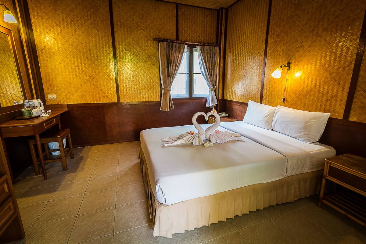 A hotel room with a neatly made bed, a desk with a chair, a window with curtains, and a wall-mounted lamp.