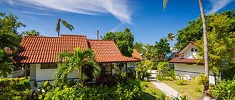 A house with a red-tiled roof, surrounded by lush greenery and a clear blue sky.