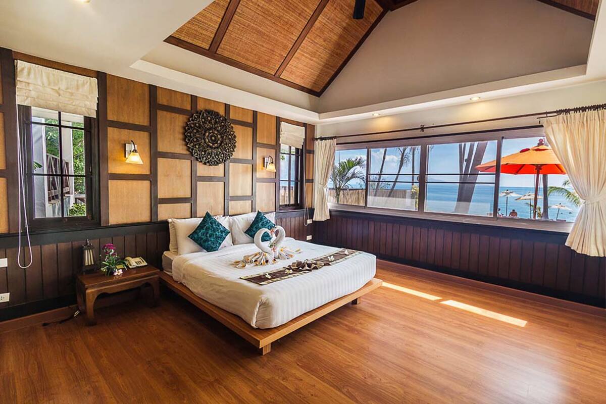 A spacious bedroom with a large bed, wooden flooring, a view of the ocean, and a ceiling with exposed beams.