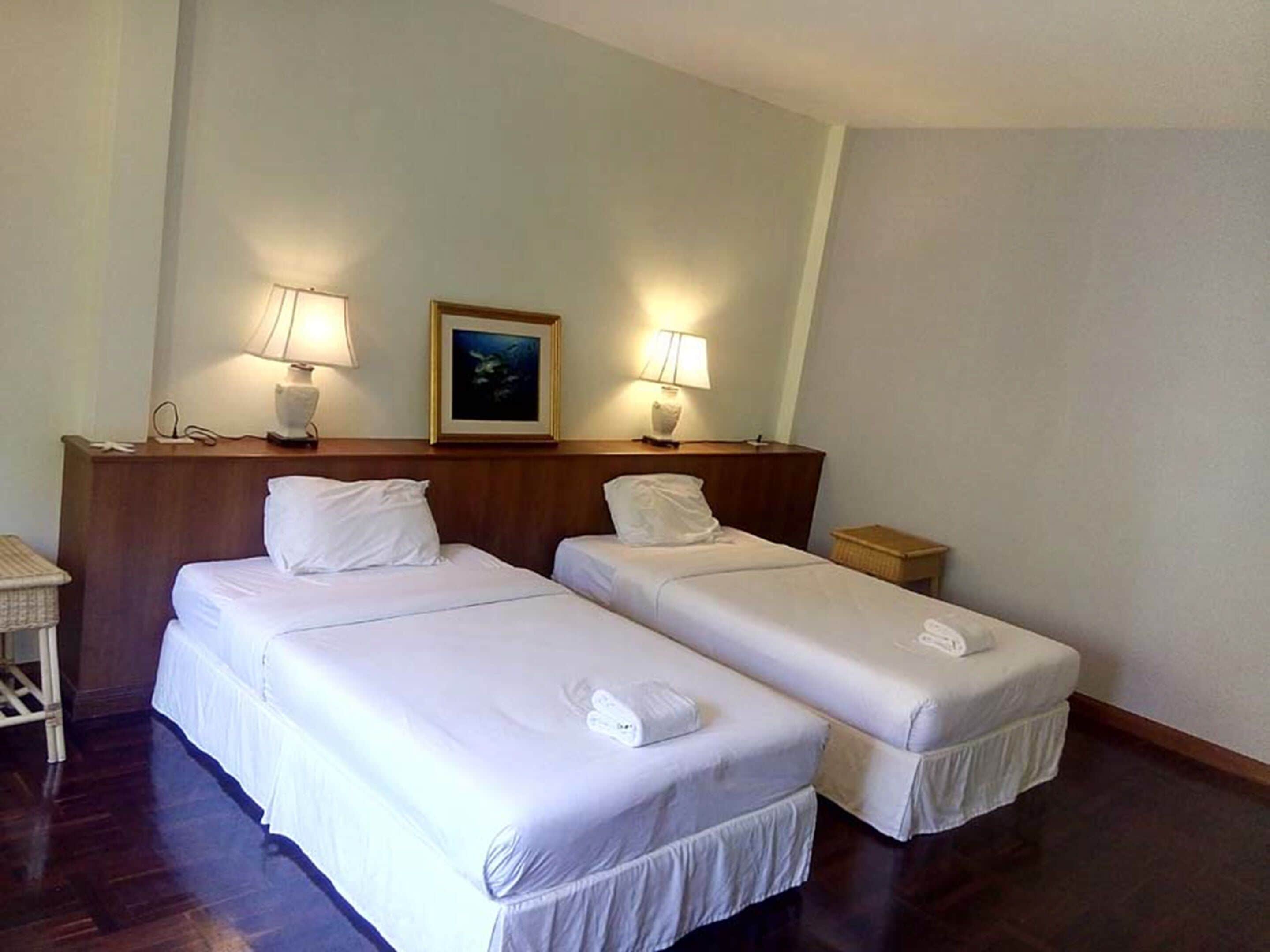 Une chambre d’hôtel avec deux lits simples, une tête de lit en bois, des lampes de chevet, un tableau encadré et une petite table de chevet.