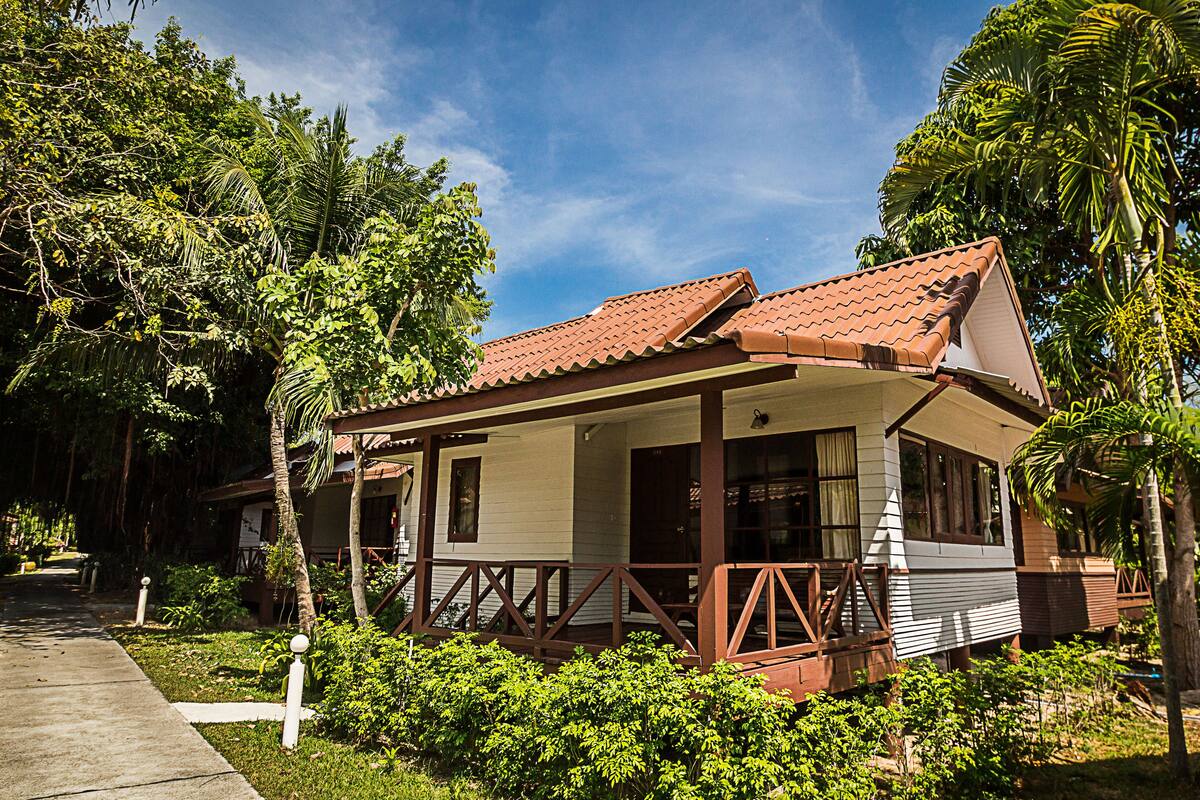 A single-story house with a tiled roof, surrounded by lush greenery and palm trees.