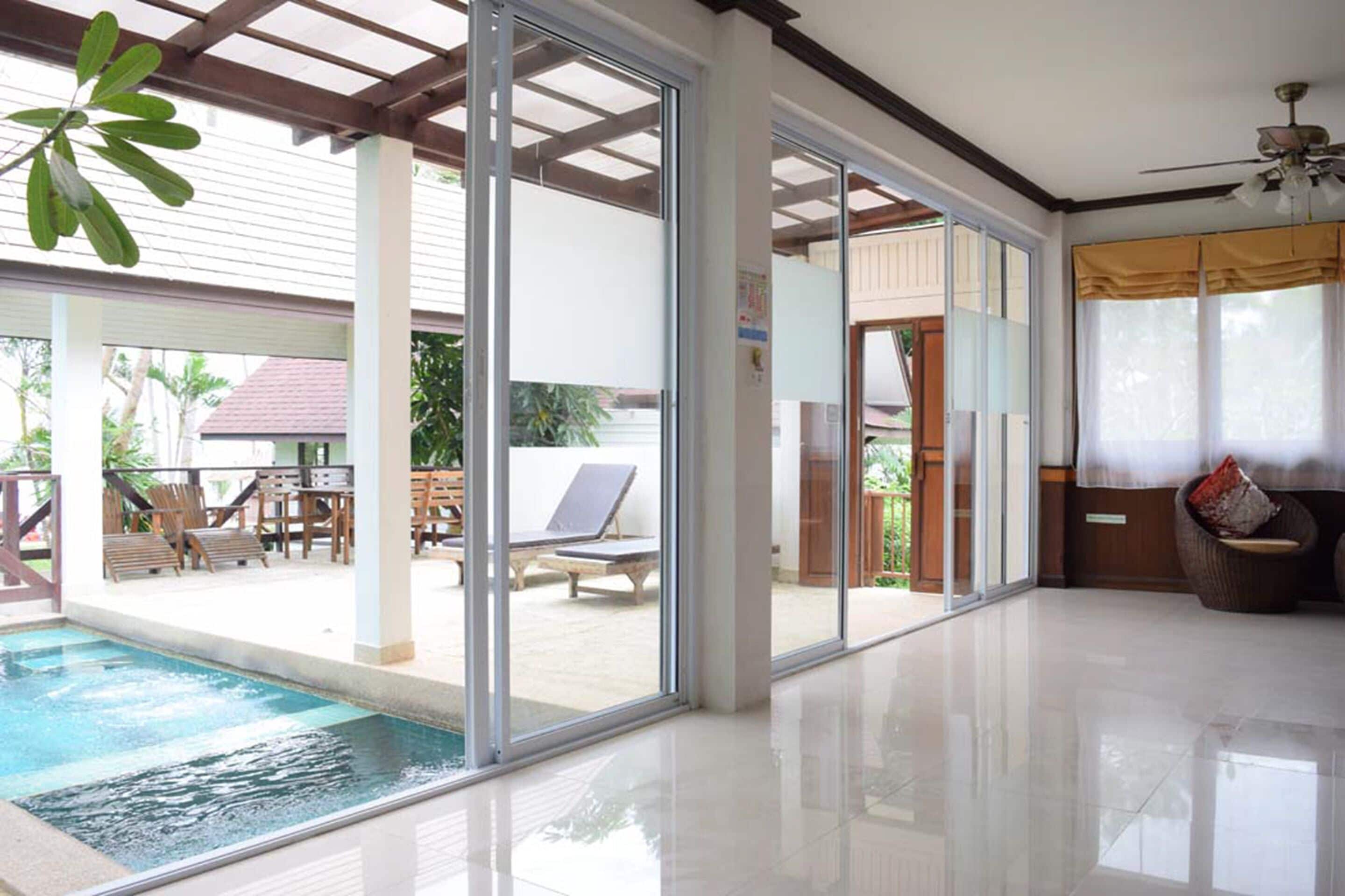 A spacious indoor area with a pool, large sliding glass doors leading to an outdoor patio with lounge chairs and a table.