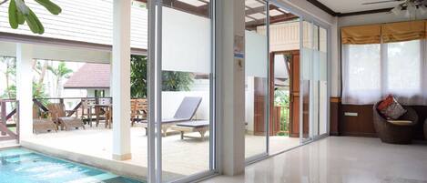 A spacious indoor area with a pool, large sliding glass doors leading to an outdoor patio with lounge chairs and a table.