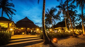 Un resort con un edificio de techo de paja, palmeras y zonas de estar al aire libre.